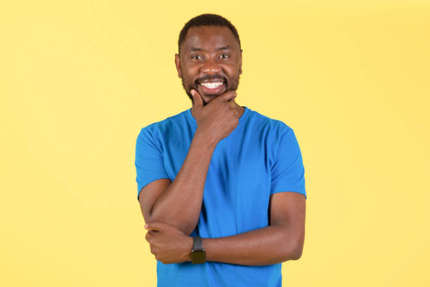 istock Black Male Posing Touching Chin Smiling Over Yellow Studio Background 1475342130