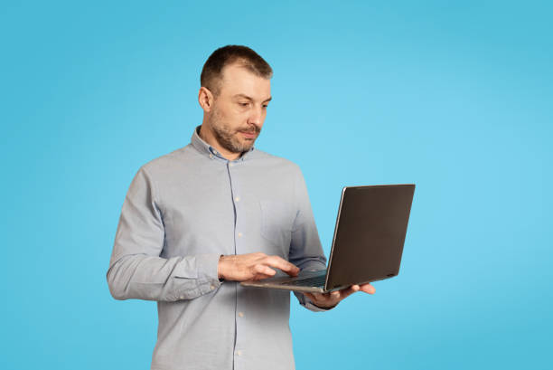 istock Middle Aged Businessman Using Laptop Computer Working Online, Blue Background 1475342310