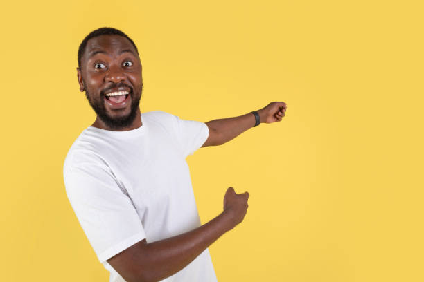 istock Excited Black Man Pointing Fingers Aside Over Yellow Studio Background 1475342344