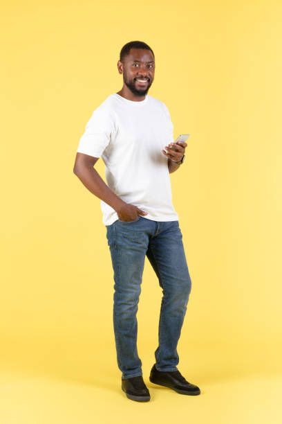 istock Cheerful Black Man Using Smartphone Standing On Yellow Background, Vertical 1475342392