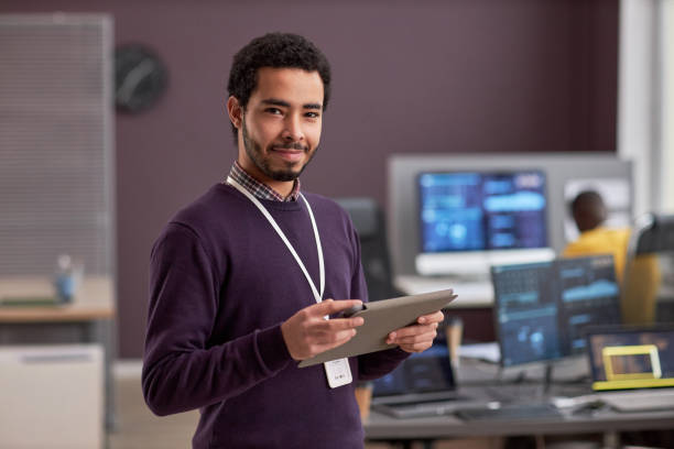 lächelnder software-ingenieur mit einem digitalen tablet in der hand, während er im tech-büro steht - seventyfour stock-fotos und bilder