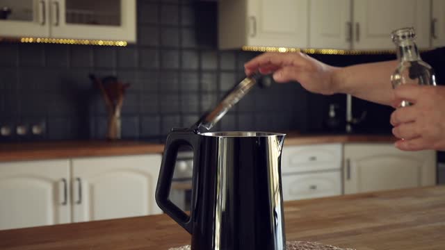 Woman pouring natural destilled acid white vinegar in electric kettle to remove boil away the limescale. Descaling a kettle, remove scale concept. Home kitchen background.