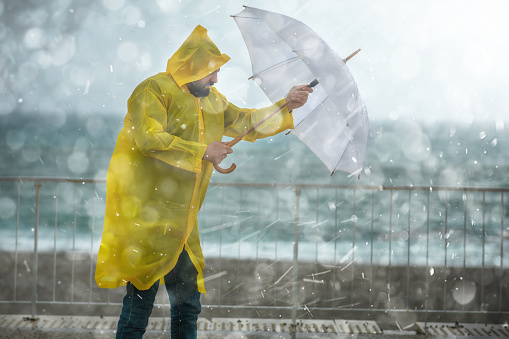 Businessman hand holding yellow umbrella over crowd on blurry dull sky background. Risk, protection and safety concept