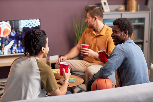 Diverse group of men watching sports match on TV at home and drinking beer