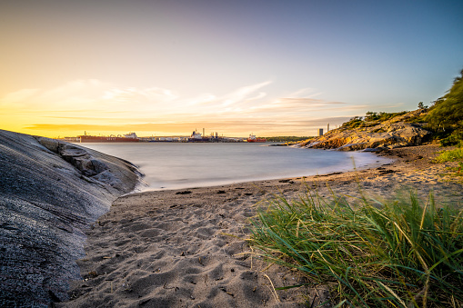 Gothenburg, Sweden - July 13 2022: Long exposure of a small sand beach across from an oil terminal.
