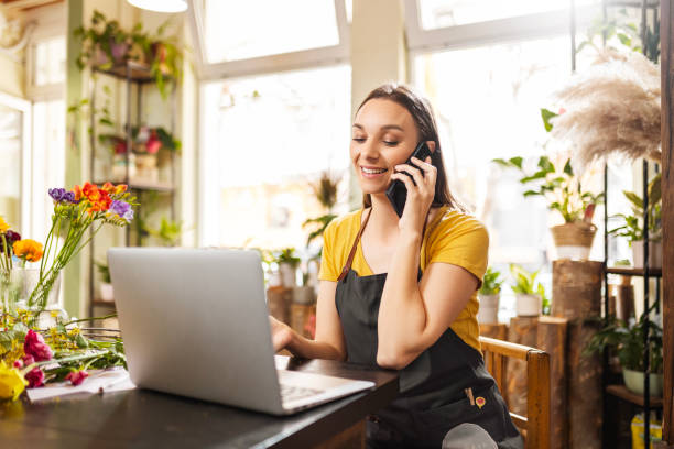 istock Female florist on phone with client writing down order on laptop 1475354920