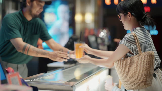 Asian  mother and her son buying popcorn from cinema bar counter.Asian bartender serving  in front bar counter for popcorn before movie show time .