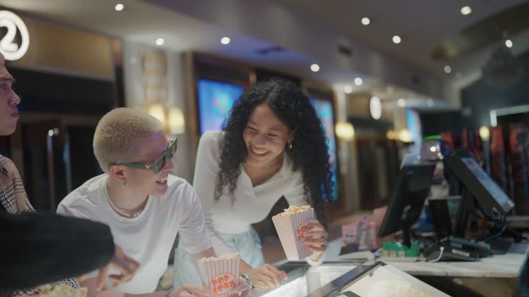 Asian group of friends at the cinema counter bar stand talking and buying popcorn for the movie.