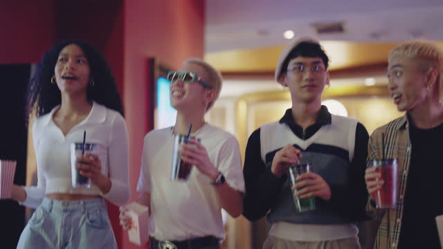 Shot of happy friends holding a popcorn ,drinks and chatting while walking to watch movie at cinema.