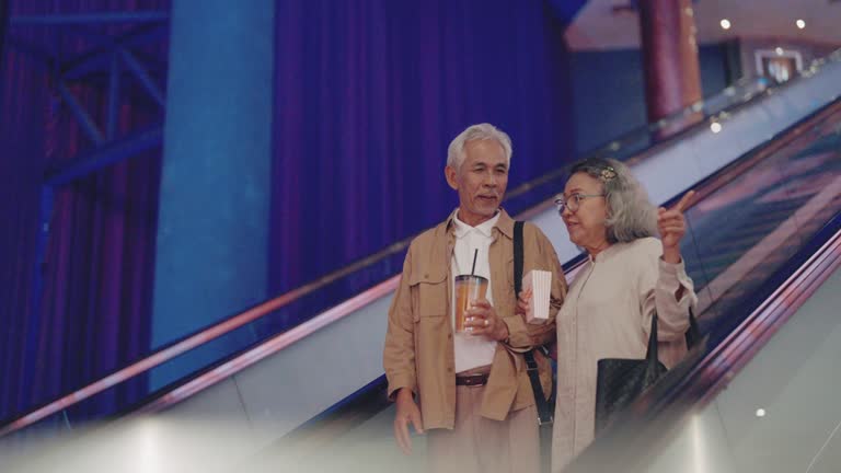 The senior asian couple talked about their recent movie as they walked down the escalator from the movie theater.