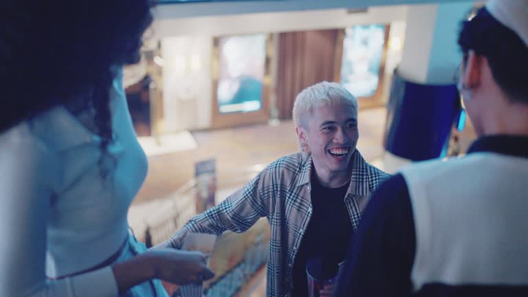 Asian three cheerful diverse friends going down escalator in cinema  and having conversation.