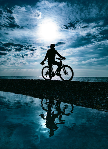 dark silhouette of a guy on a mountain bike against the background of the sea and beautiful textures of clouds