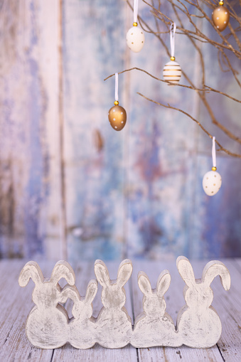 Five boho Easter bunnies and Easter eggs hanging on a natural branch on blue vintage background. Creative color editing with added grain. Very soft and selective focus. Part of a series.
