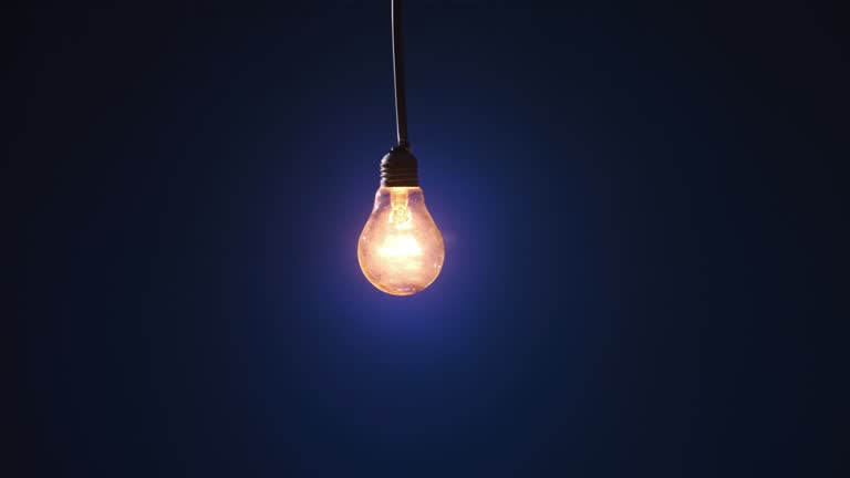 Incandescent Lamp on Wire Sways and Lights Up with Flickers on Blue Background