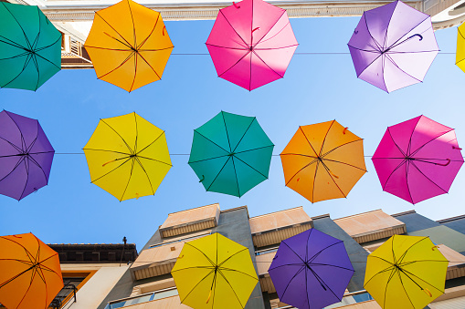 Multi-colored umbrellas hang on the street along the houses against the sky.