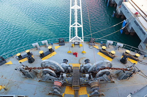The bow of a cargo ship moored to the pier, with mooring winches on the deck, top view.