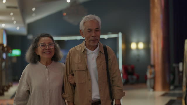 Senior couple walks arm in arm and talks on the way before entering the cinema.