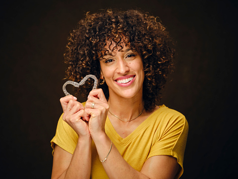 A happy young woman holding invisible clear teeth aligners.