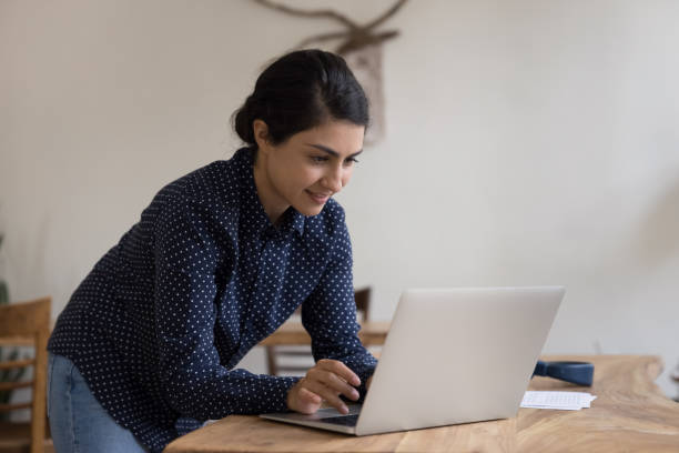istock Focused happy young Indian laptop user woman standing at workplace 1475369643