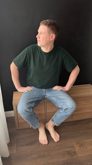 young man, emotions, laughter, smile, thoughtful, cheerful, in a green T-shirt, blue jeans, hands, bare feet