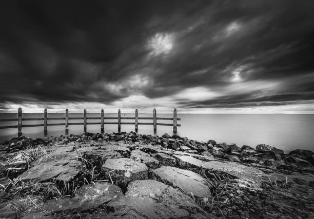 Lake view at dark time with heavy clouds and stormy winds. Stretch dam in the lake with a wooden pile construction