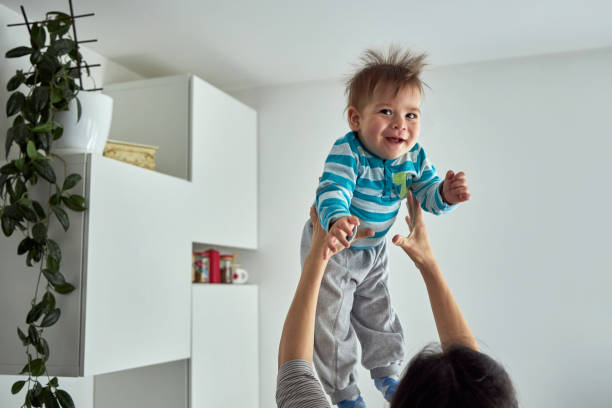 Young mom throwing excited laughing baby boy up in air and catching stock photo
