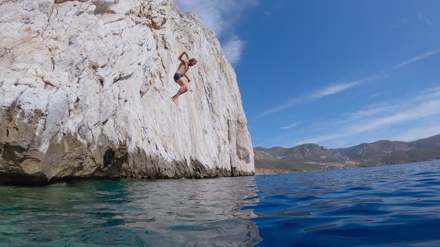 Man jumps from high cliff into deep blue water