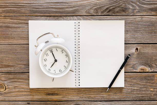 istock White blank notepad and alarm clock on wooden background, flat lay. 1475377329