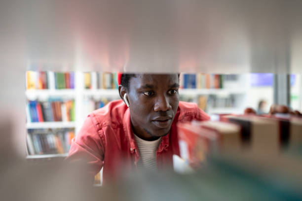 Black student man choose book in college library learning in university preparing for test or exam