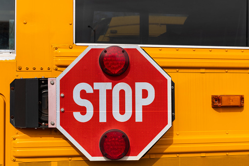 A big red stop sign on the side of a yellow school bus.