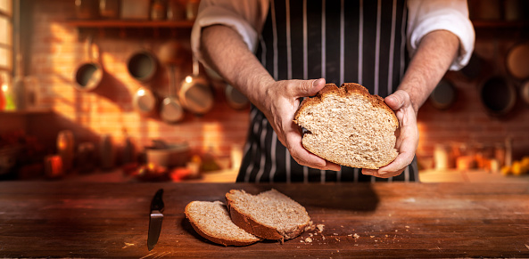 Baker presenting loaf of bread on wooden table in vintage kitchen