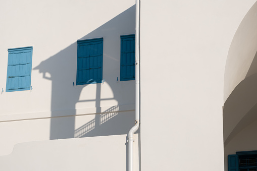 white painted walls and blue windows with shadows on a sunny day. Traditional Greek or religion Abstract Architecture concept.
