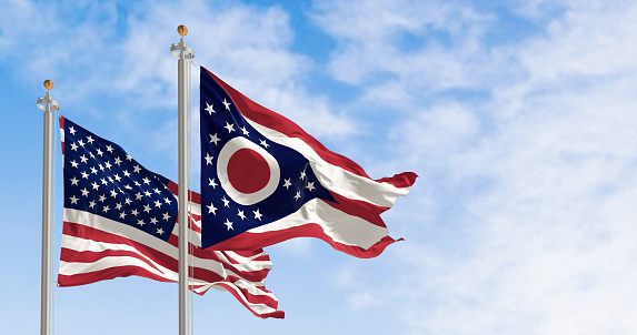 The Ohio state flag waving along with the national flag of the United States of America. In the background there is a clear sky. 3D illustration render. Rippled textile