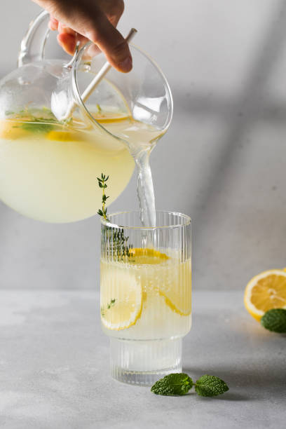 istock Lemonade with fresh lemon slices is poured from a jug into a glass. Summer refreshing drink with lemon. 1475390558
