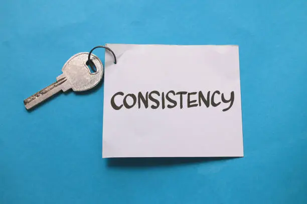 Photo of Consistency is the key, text words typography written on paper against blue background, life and business motivational inspirational