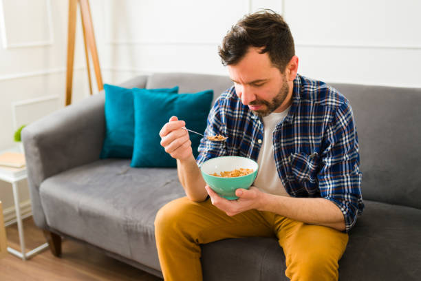 istock Happy man eating cereal for breakfast on the sofa 1475394211