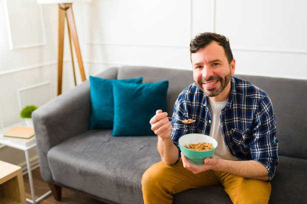 istock Smiling cheerful man eating breakfast relaxing on the sofa 1475394218