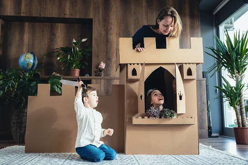 Mother And Children Playing Role Play Game At Home With Castle Made Of Cardboard