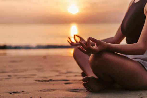 istock Woman meditating on the beach at sunset 1475415338