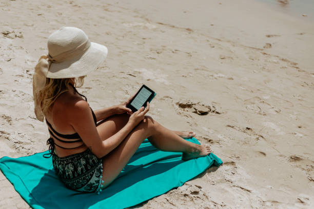 istock Woman with an e-reader on vacation at the beach reading a book 1475421118