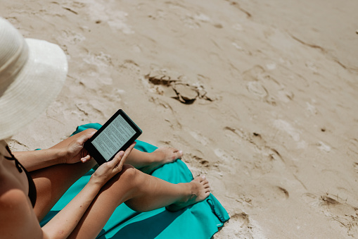 Woman with an e-reader on vacation at the beach reading a book
