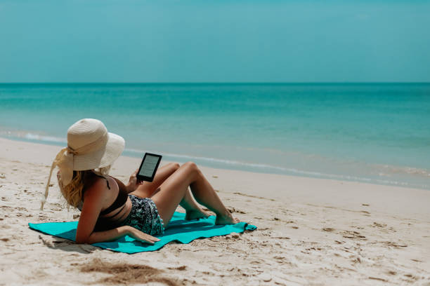 Woman relaxes while reading a book on her ereader on the beach