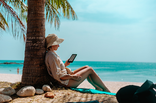Woman with an e-reader on vacation at the beach reading a book