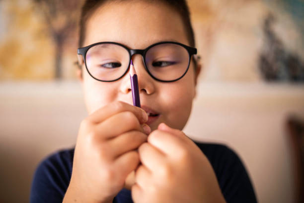 istock Smart young Asian boy wearing glasses squints at the pencil. The vision diseases problem. 1475423288