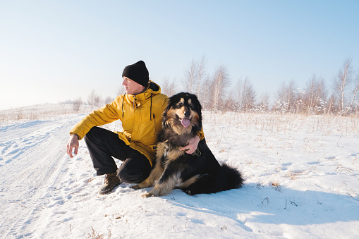 Male in yellow coat walking with his big black dog on winter background. Family winter activity with pet on sunny day outdoor. Mongolian dog breed.