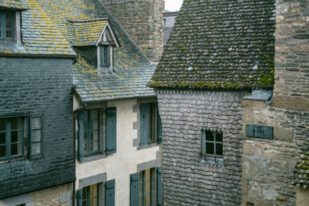 Mont Saint-Michel Abbey and Slate Roof - Low angle view of the Gothic abbey and spire of Mont Saint-Michel, seen over the weathered slate roof of a historic village building in France.
