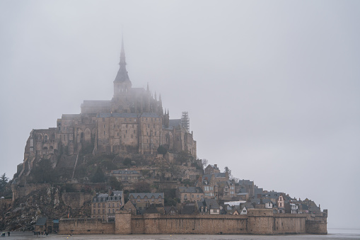 Mont-Saint Michel,France,March 11 2023: Tourists walking around Mont-Saint Michel on a rainy day. Mont-Saint Michel is one of the most popular attractions in France to international tourists.