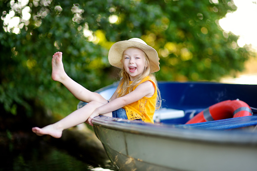Cute little girl having fun in a boat by a river at beautiful summer evening