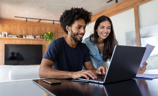 Young Brazilian couple at home paying bills online on a laptop computer - home finances concepts