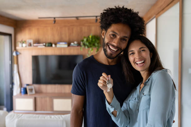 pareja feliz comprando una casa y sosteniendo las llaves mientras sonríe - pareja de mediana edad fotografías e imágenes de stock